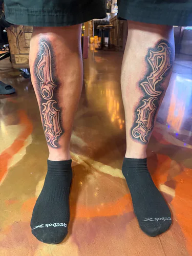 Bold 1979 ornate lettering tattoo across both lower legs by Chyloe at Golden Tarot Ink Club