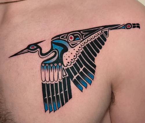 Bold graphic bird in flight across the chest in black with blue and red, a tattoo by Chyloe at Golden Tarot Ink Club