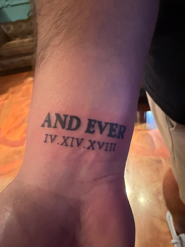 Bold AND EVER lettering with a roman numeral date, a forearm tattoo by Stevo at Golden Tarot Ink Club